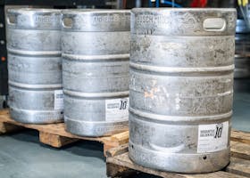 Image of metal beer kegs on wooden pallets in an indoor brewery setting, ideal for industrial storage themes.